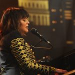 Norah Jones sits at a piano, singing into a microphone