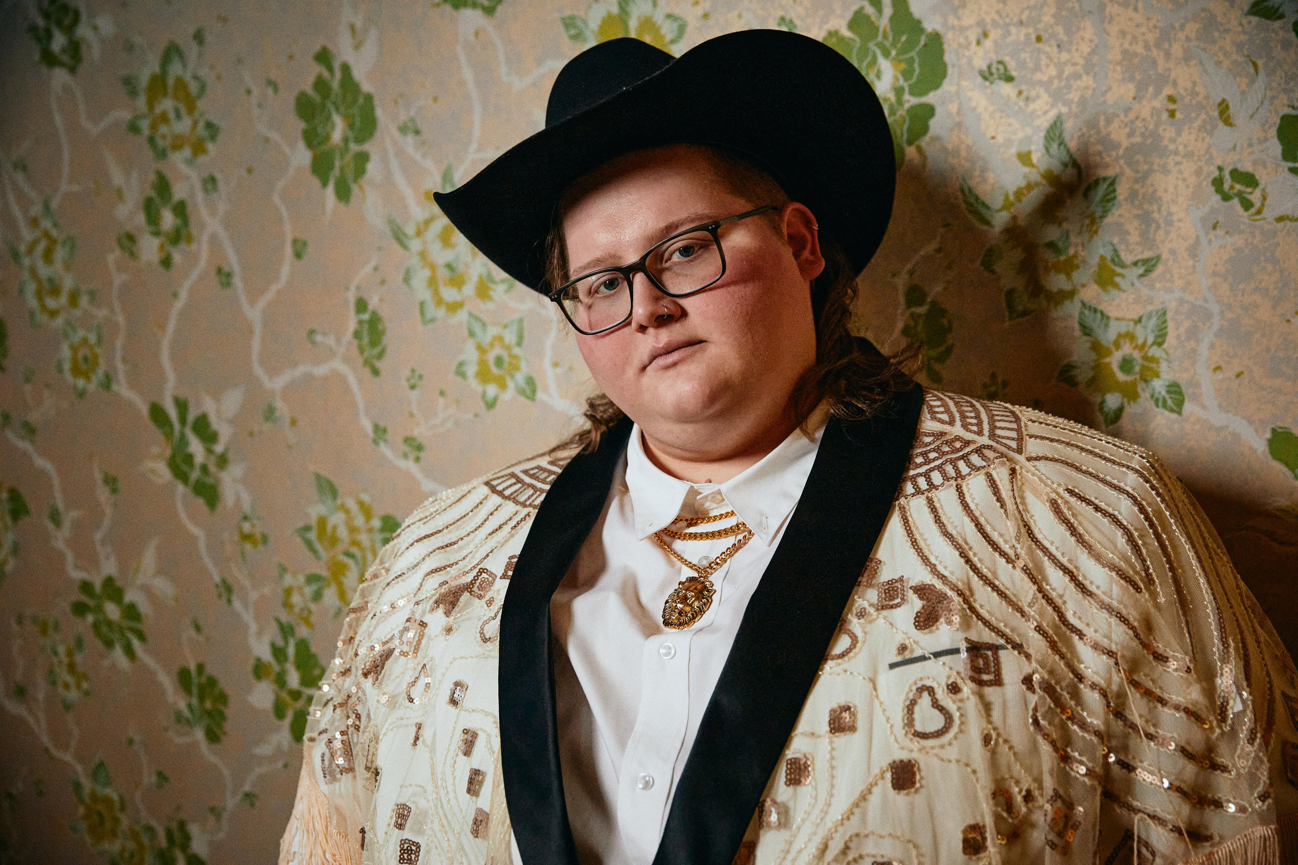 Joshua Ray Walker, wearing a cowboy hat, a flashy jacket and standing against a wallpapered wall.