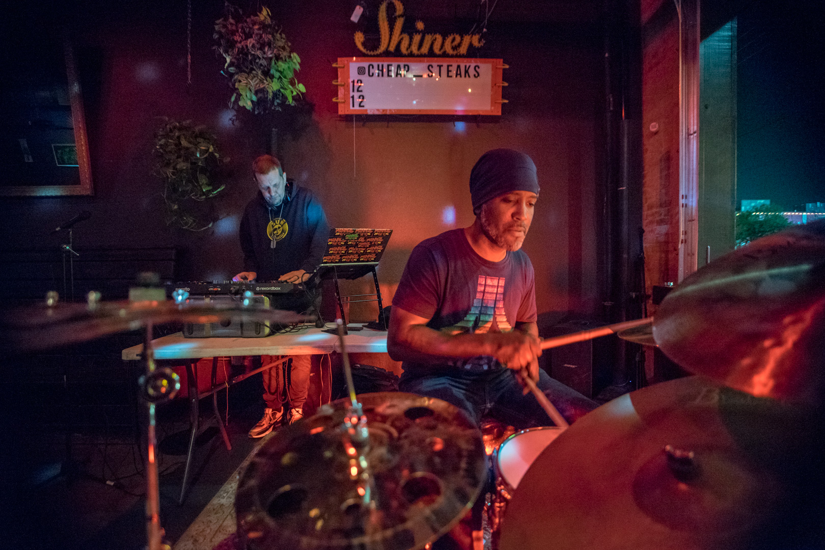 A dj and a drummer on a small stage playing together.