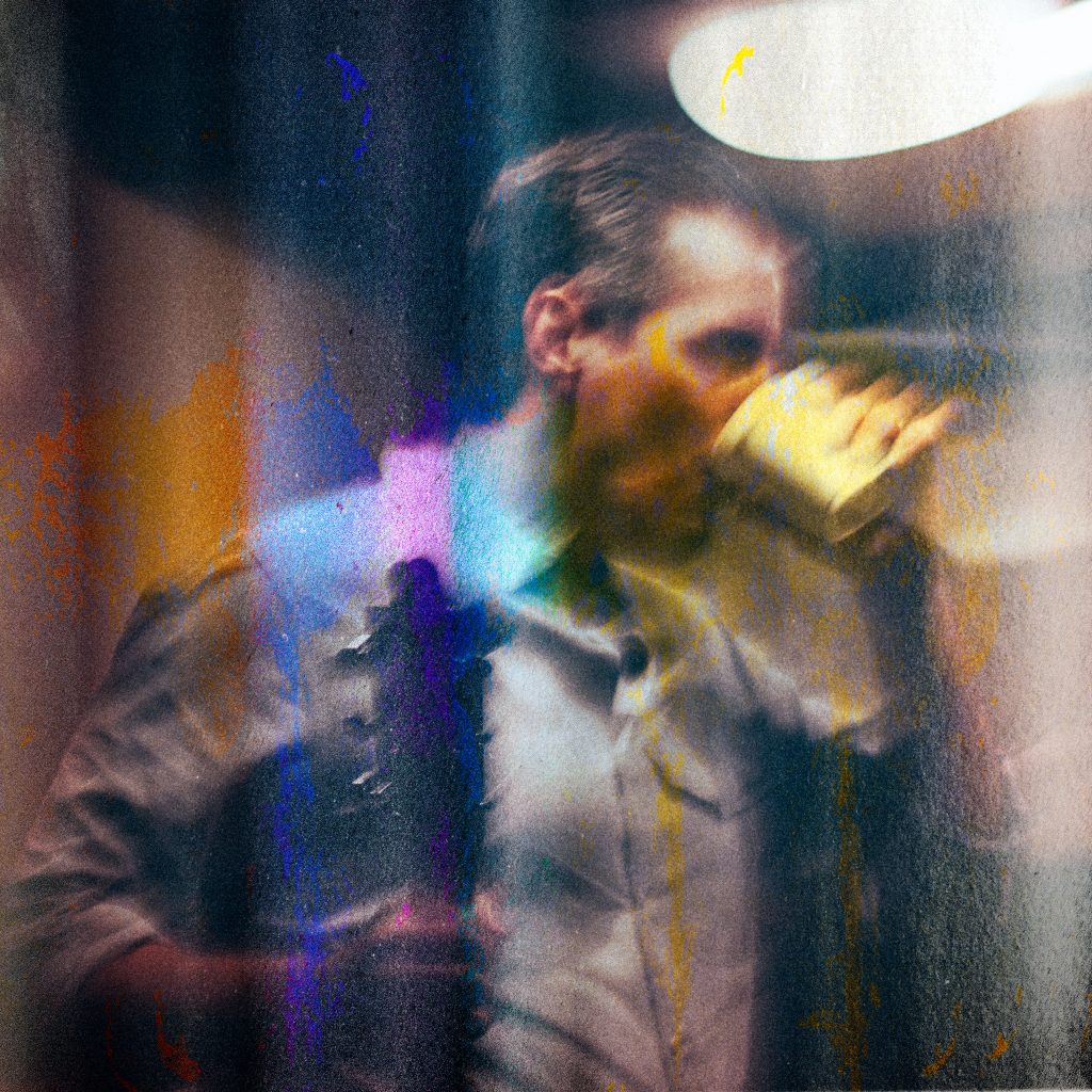 Holding an acoustic guitar, Eric Steele sips from a coffee mug in a blurry, streaky image