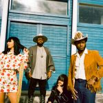 The 3 members of Khruangbin and Leon Bridges stand in front of a window with blue shutters