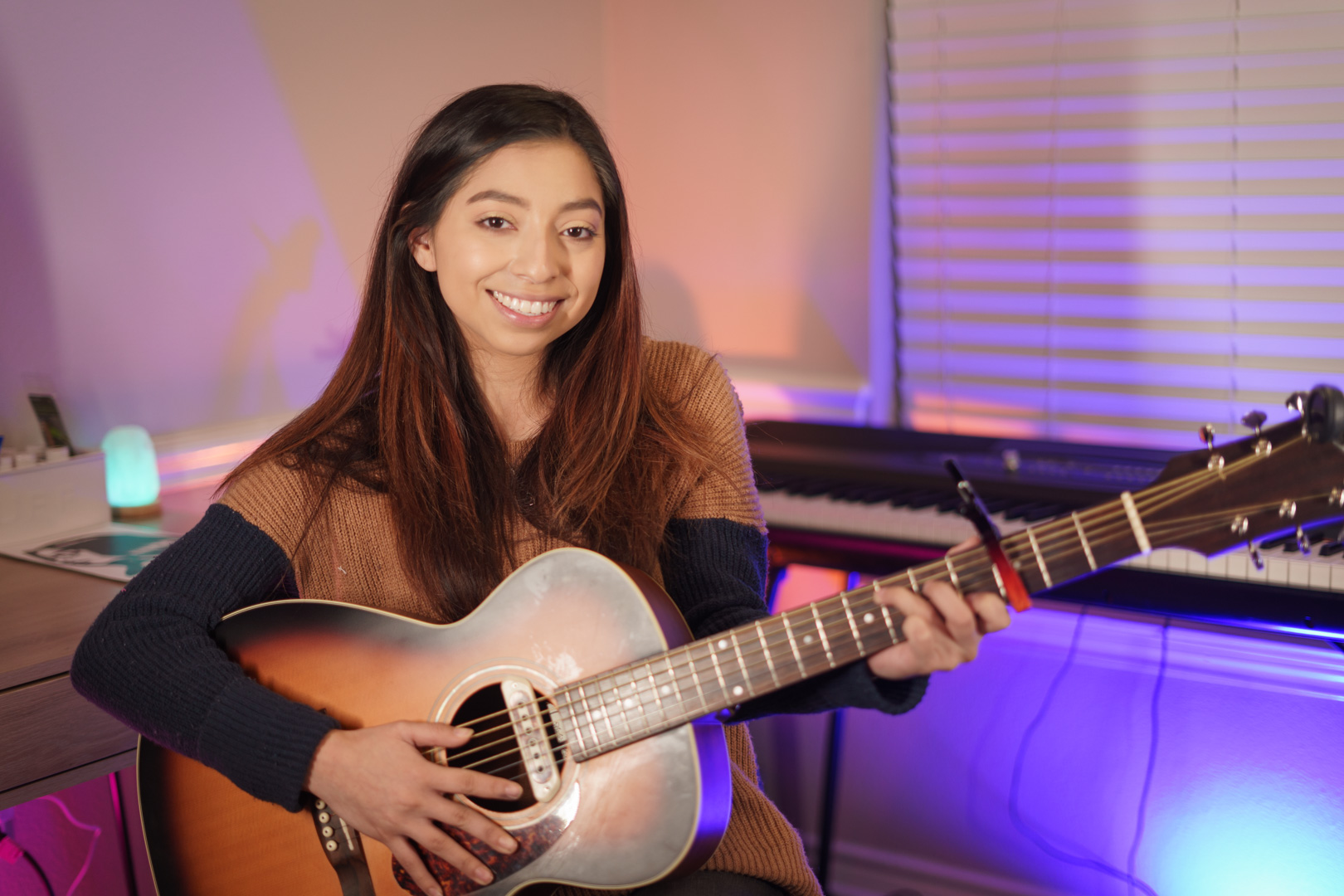 A young girl with long brown hair holds a guitar while smiling.