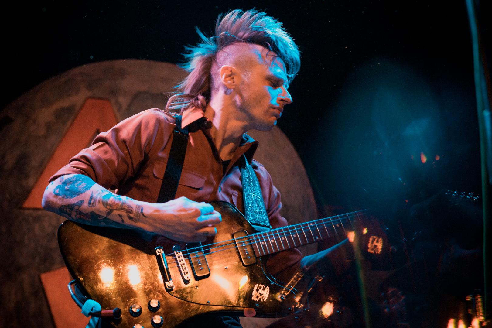 A man with guitar on stage with full mohawk