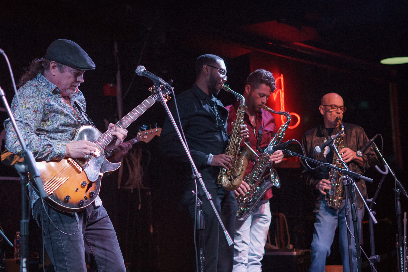 A guitar player and three saxophonists play on stage