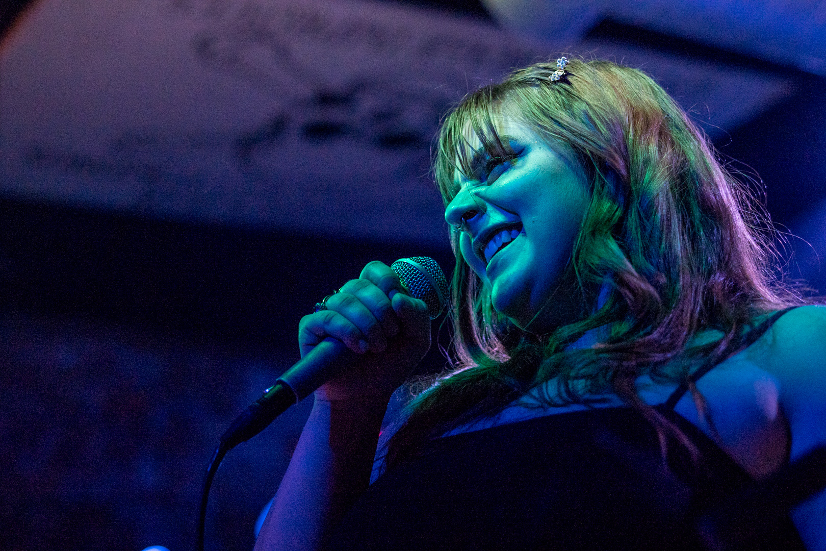 A young woman sings into a microphone while smiling
