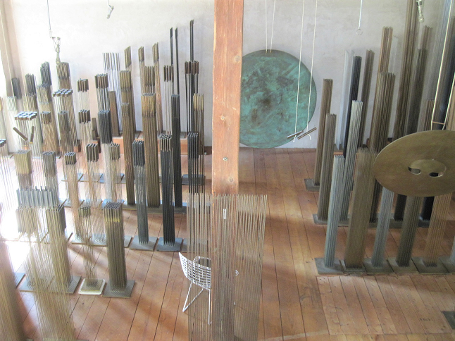 A variety of sounding sculptures are arranged inside a barn on a wooden floor