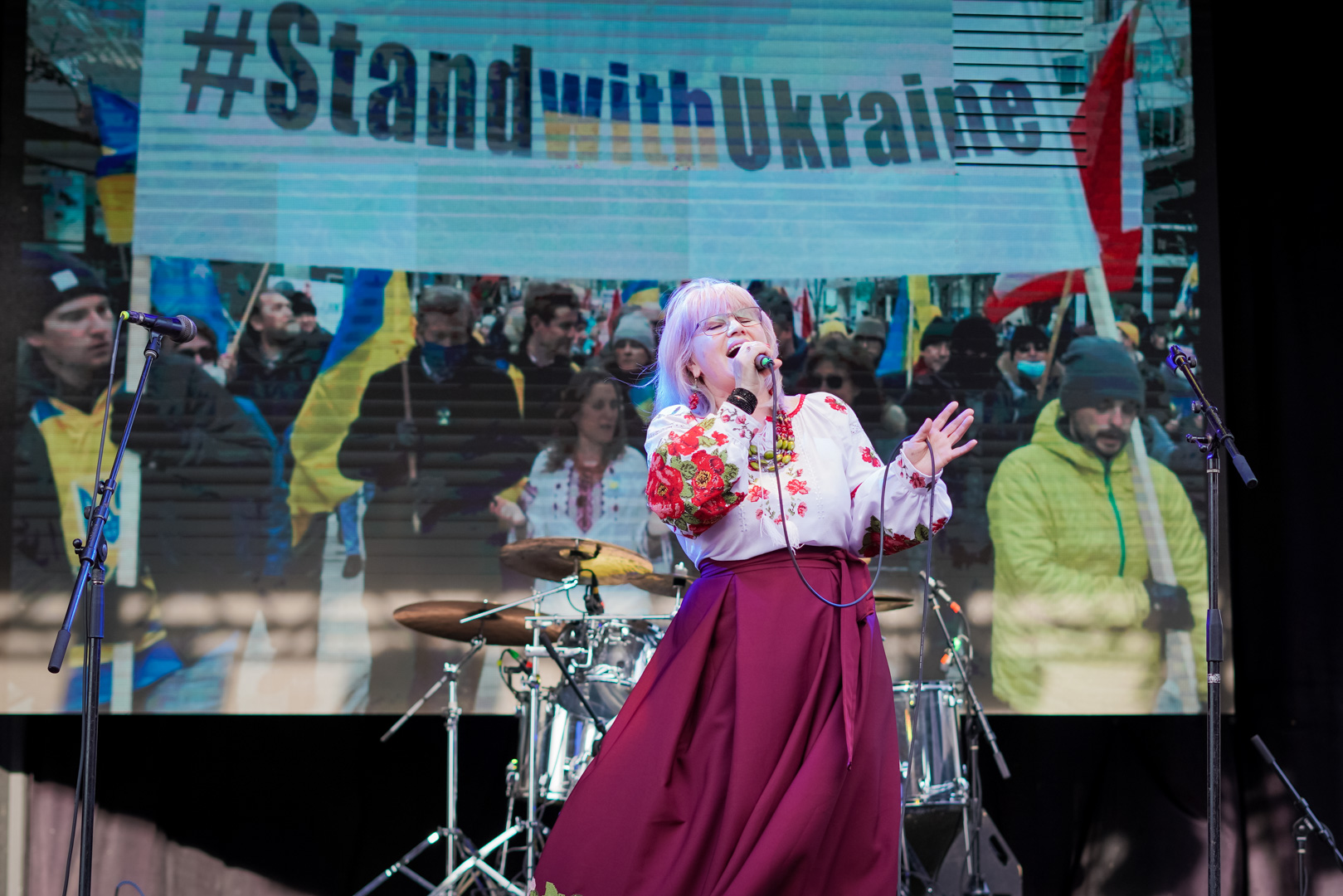 A woman sings in front of a stage with image that says "Stand with Ukraine"