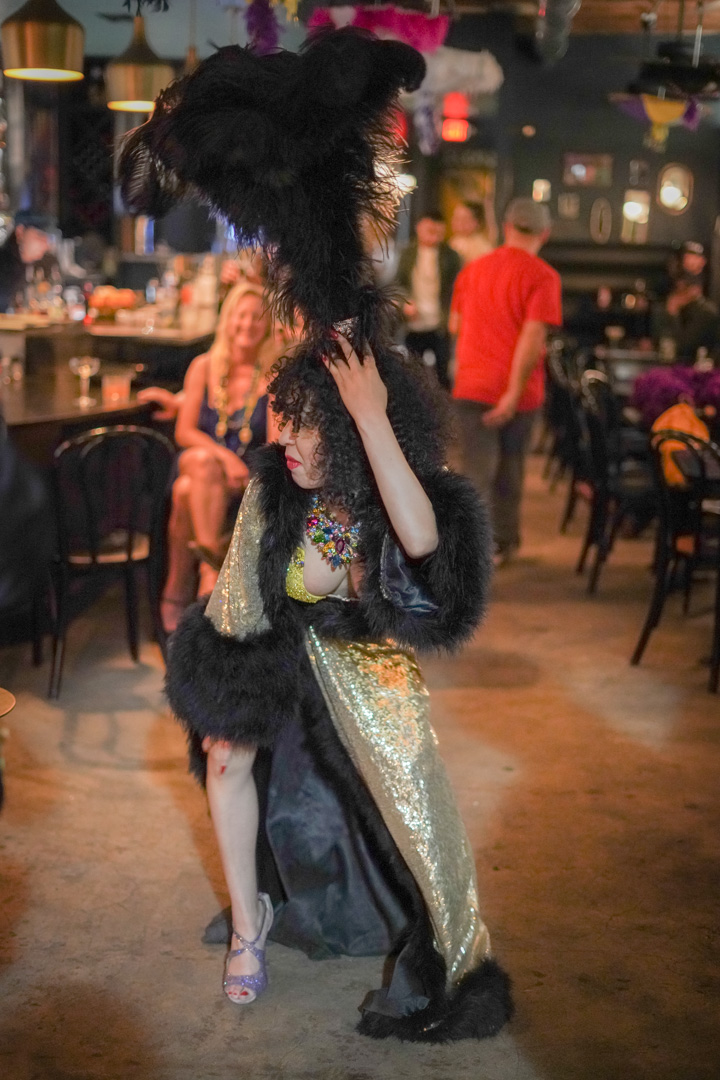 A woman in a tall feather hat and sequin robe dances