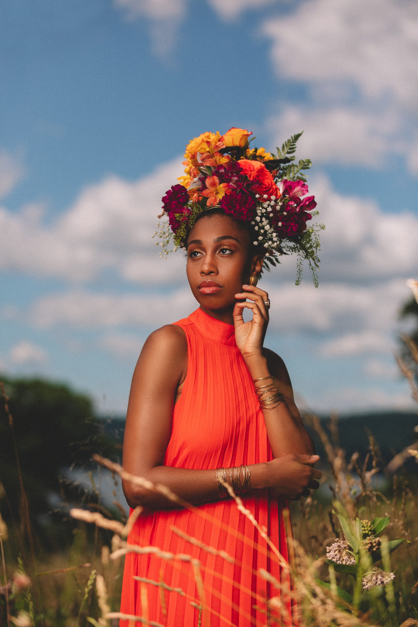 Jazzmeia Horn, standing in tall grass and wearing a bright orange dress, looks off to the left
