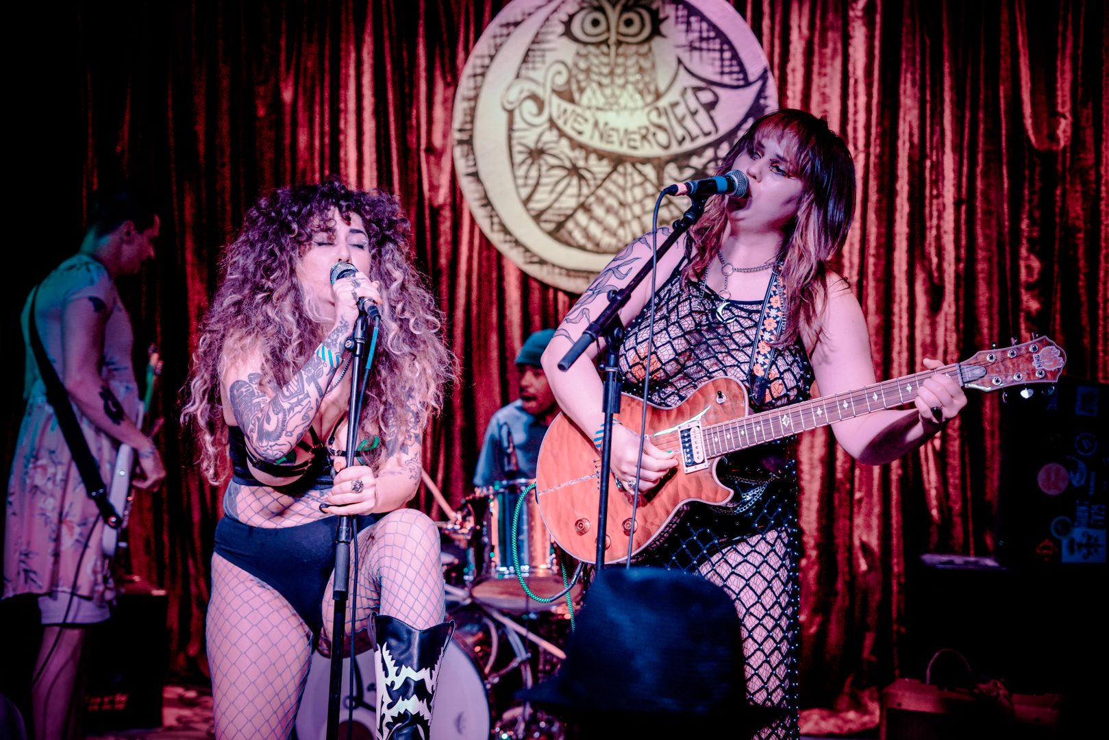 Two women sing and play guitar on stage while dressed scantily clad