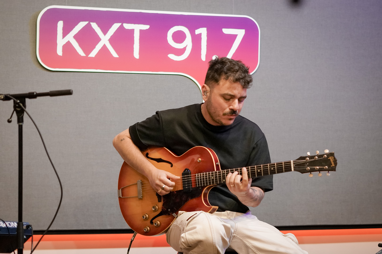 A man plays guitar in front of "KXT 91.7" sign