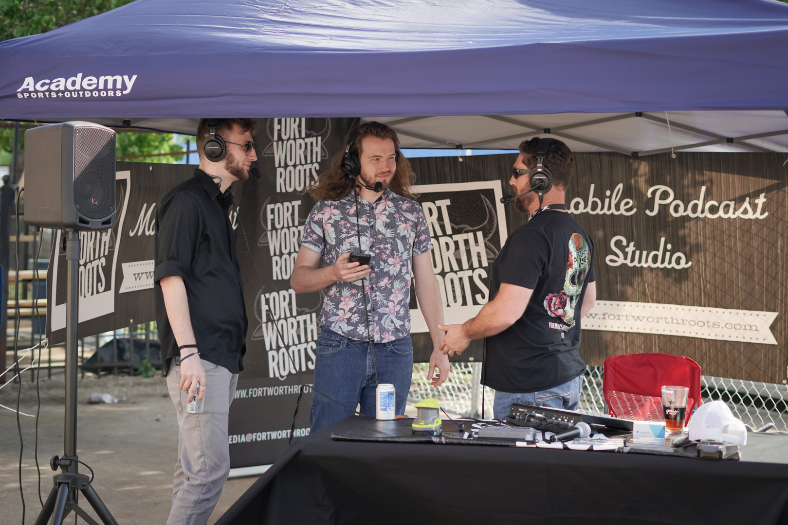 Two men interviewed by another man while standing in an outdoor mobile podcast booth