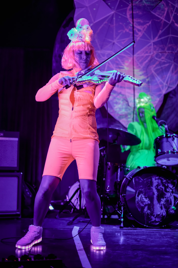 A woman in neon pink outfit plays violin