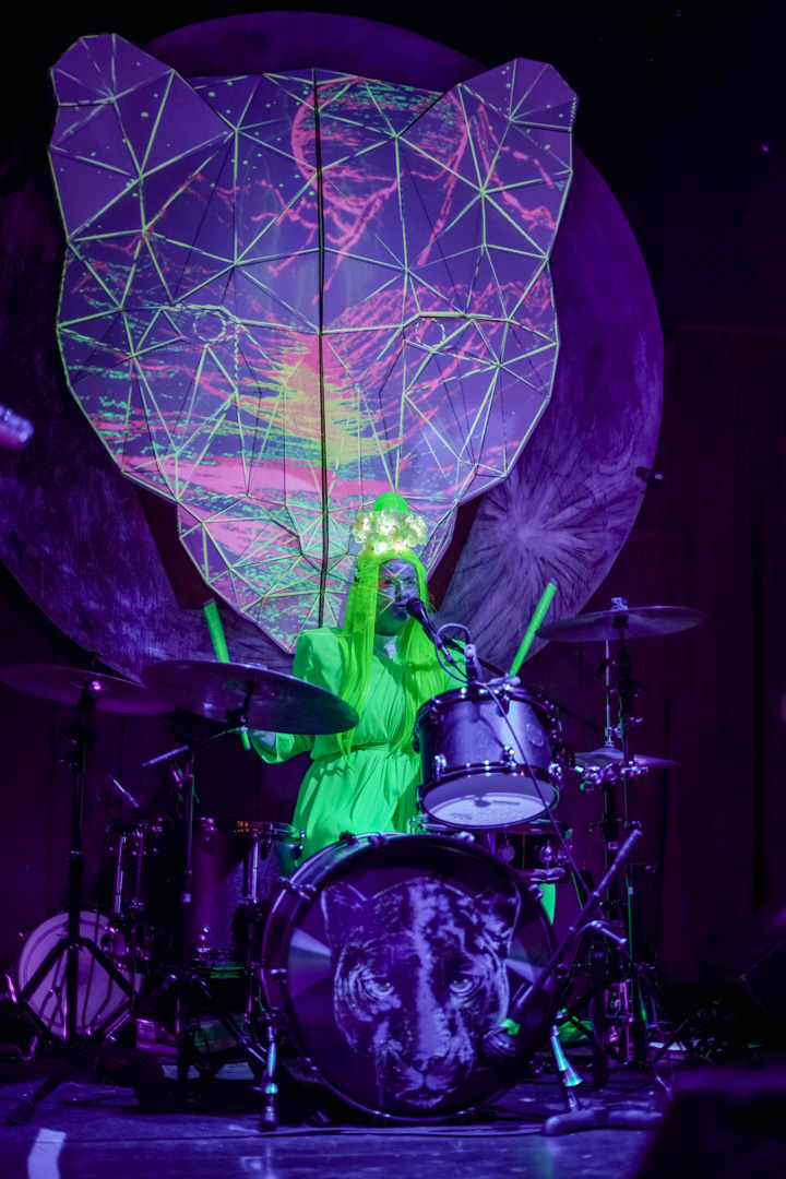 A woman in neon green outfit plays drums