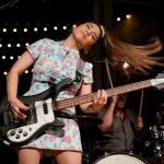 A young woman playing bass mid-hair flip