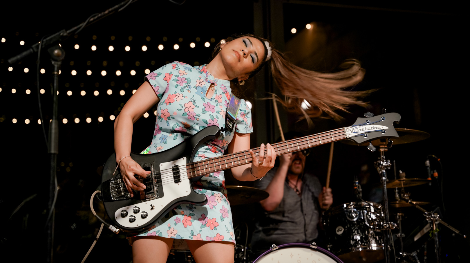 A young woman playing bass mid-hair flip