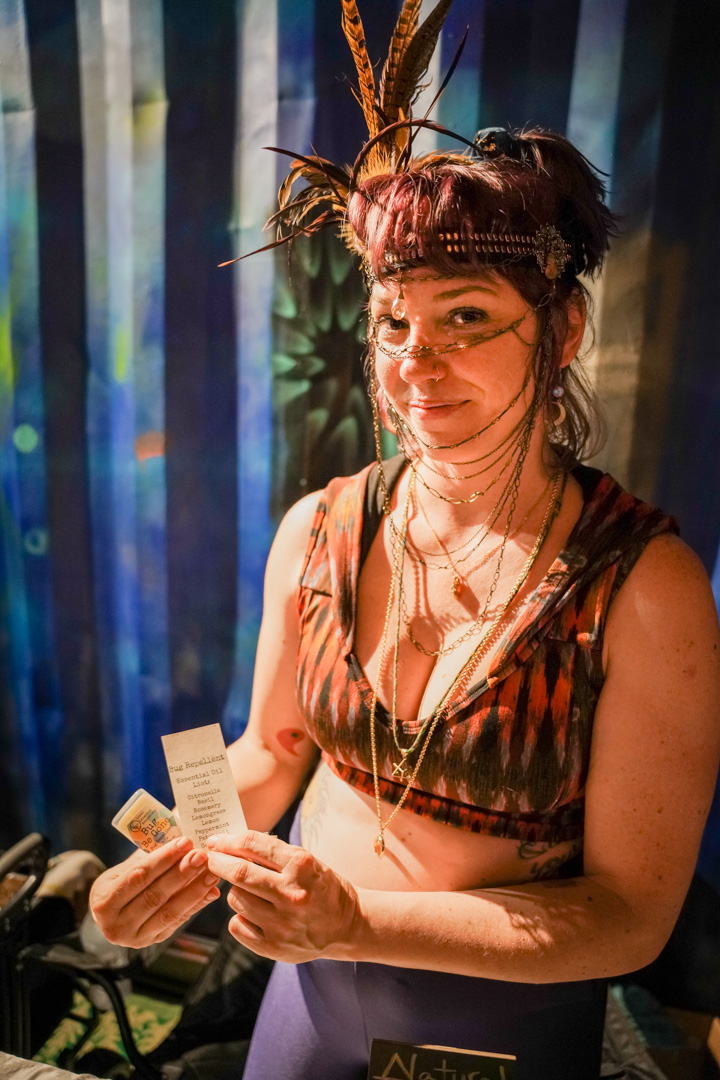 A woman in a bohemian head piece holding a small balm product