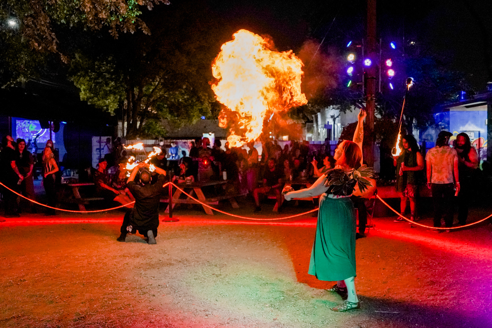 A woman blows fire in front of a crowd outdoors