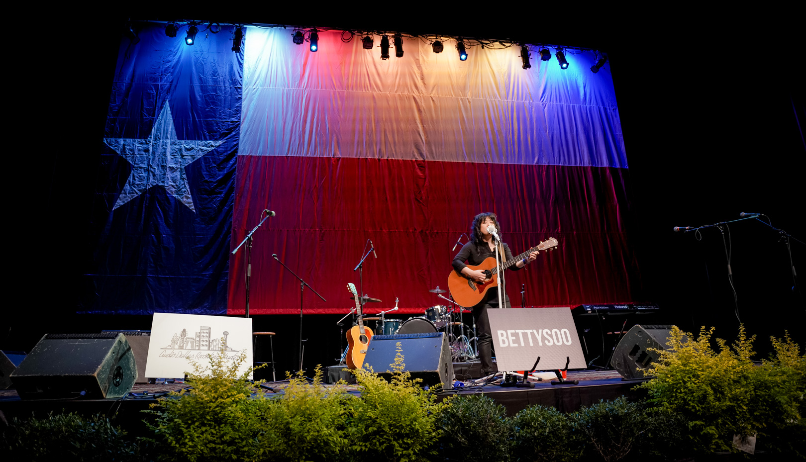 A woman plays guitar in front of a giant Texas flag on stage
