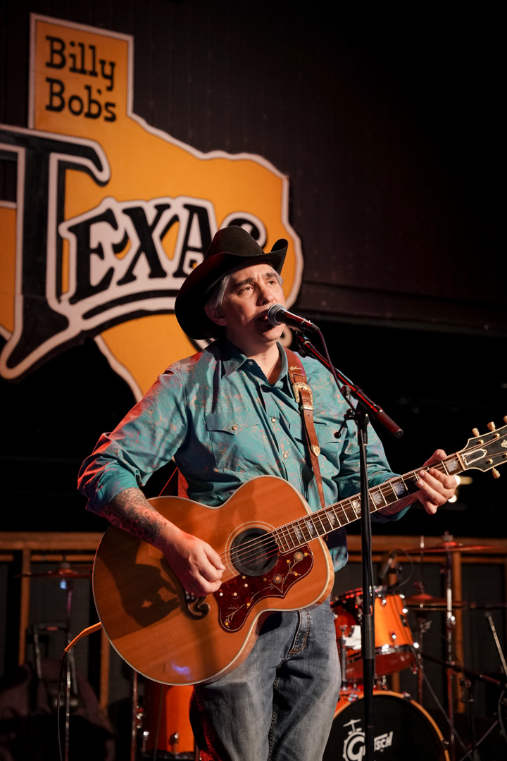 A man plays guitar on stage wearing a cowboy hat