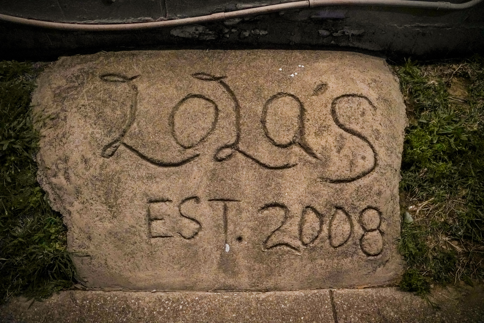 A piece of sidewalk cement with "LOLa'S EST. 2008" carved in it
