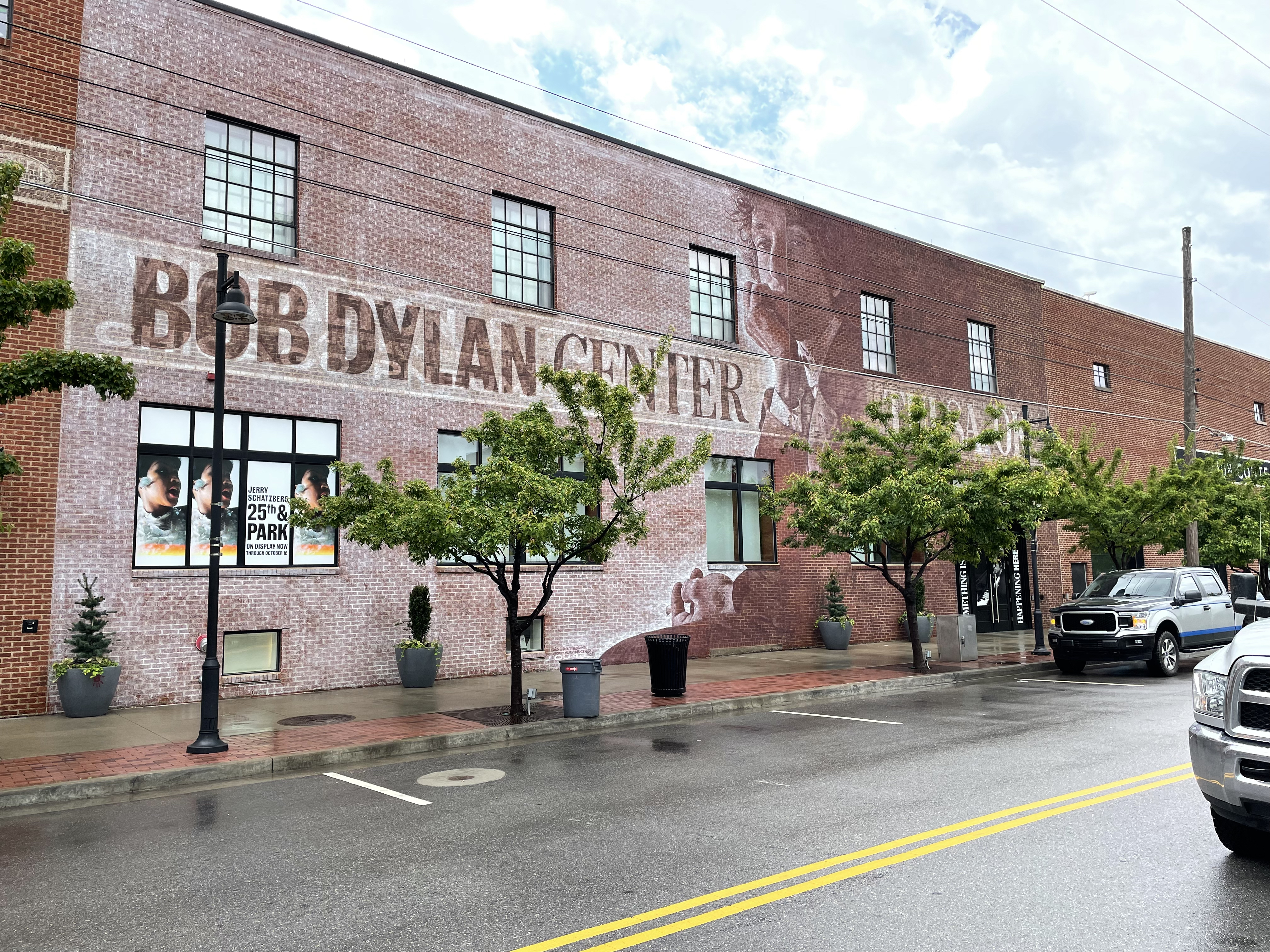 A brick facade, with the words "Bob Dylan Center," is flanked by some green trees