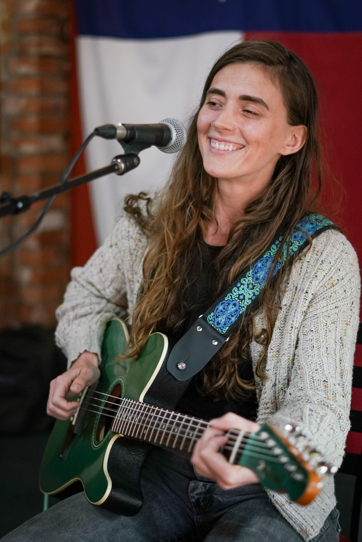 A young woman smiles and plays guitar