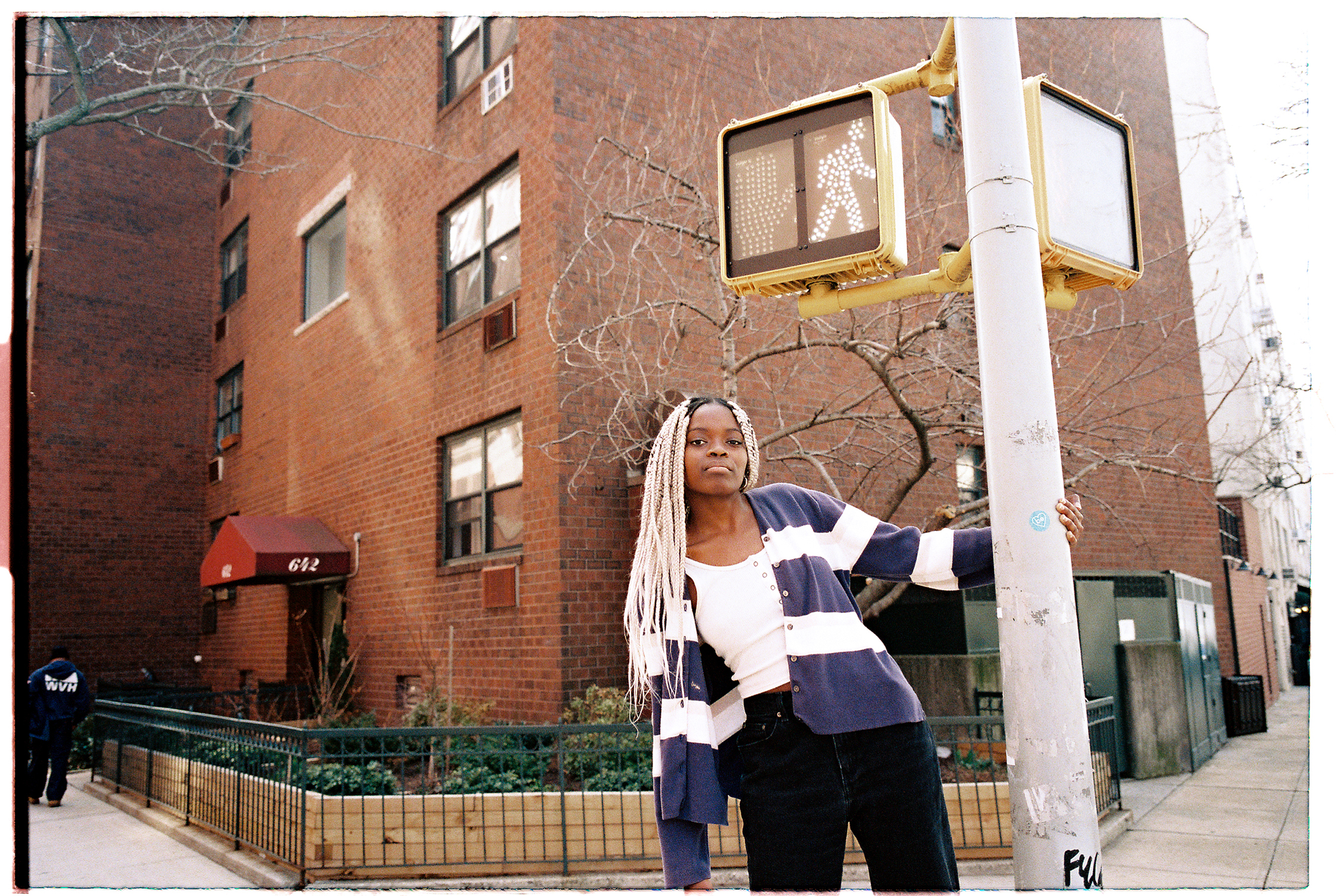 Wearing a black and white striped sweater, Hannah Jadagu stands next to a light pole on the street