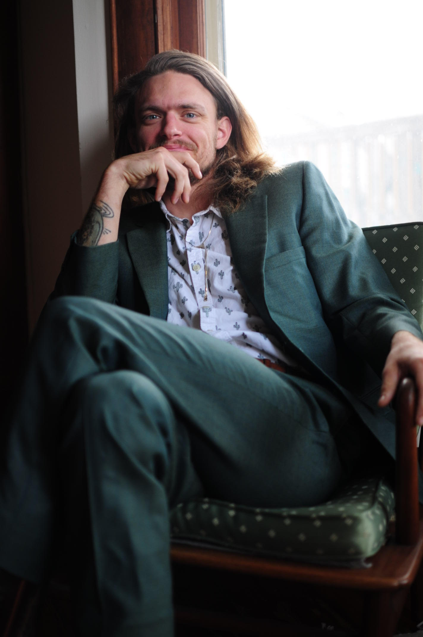 Jon Ruhl, wearing a green suit, sits in front of a window