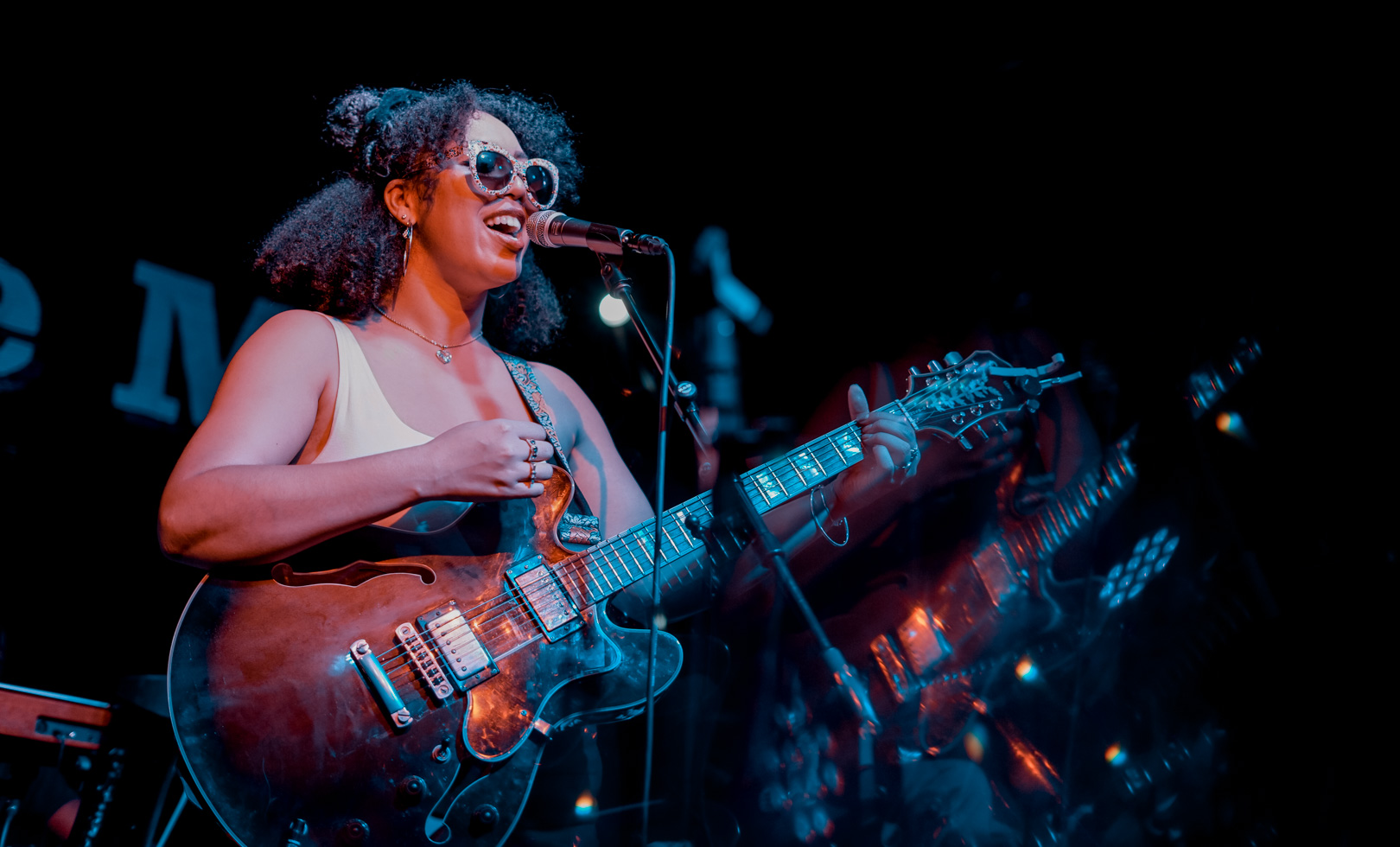 A woman sings and plays guitar on stage wearing sunglasses