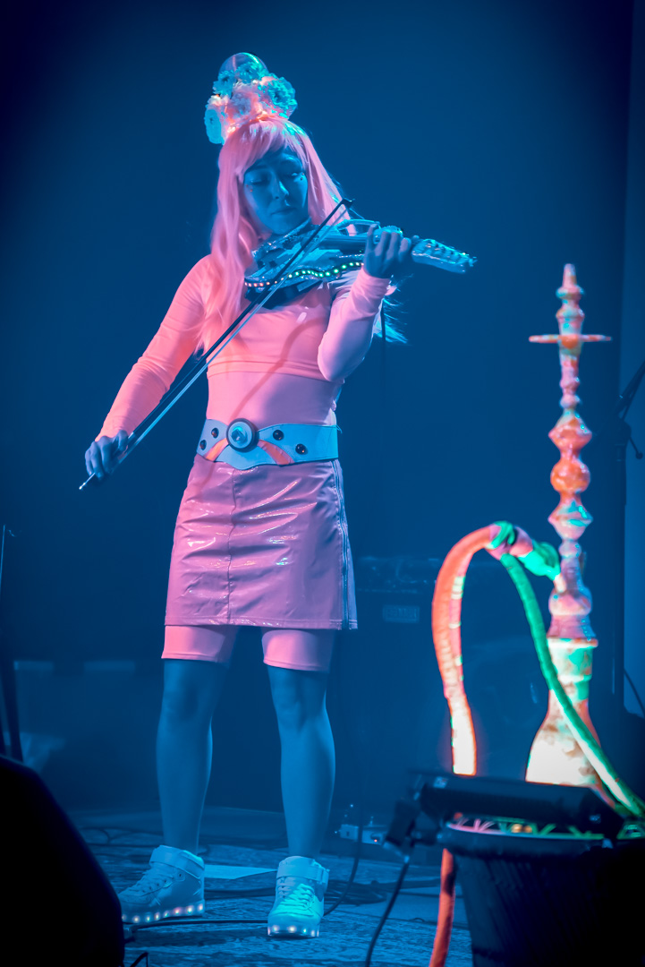 A woman in pink neon outfit playing violin on stage