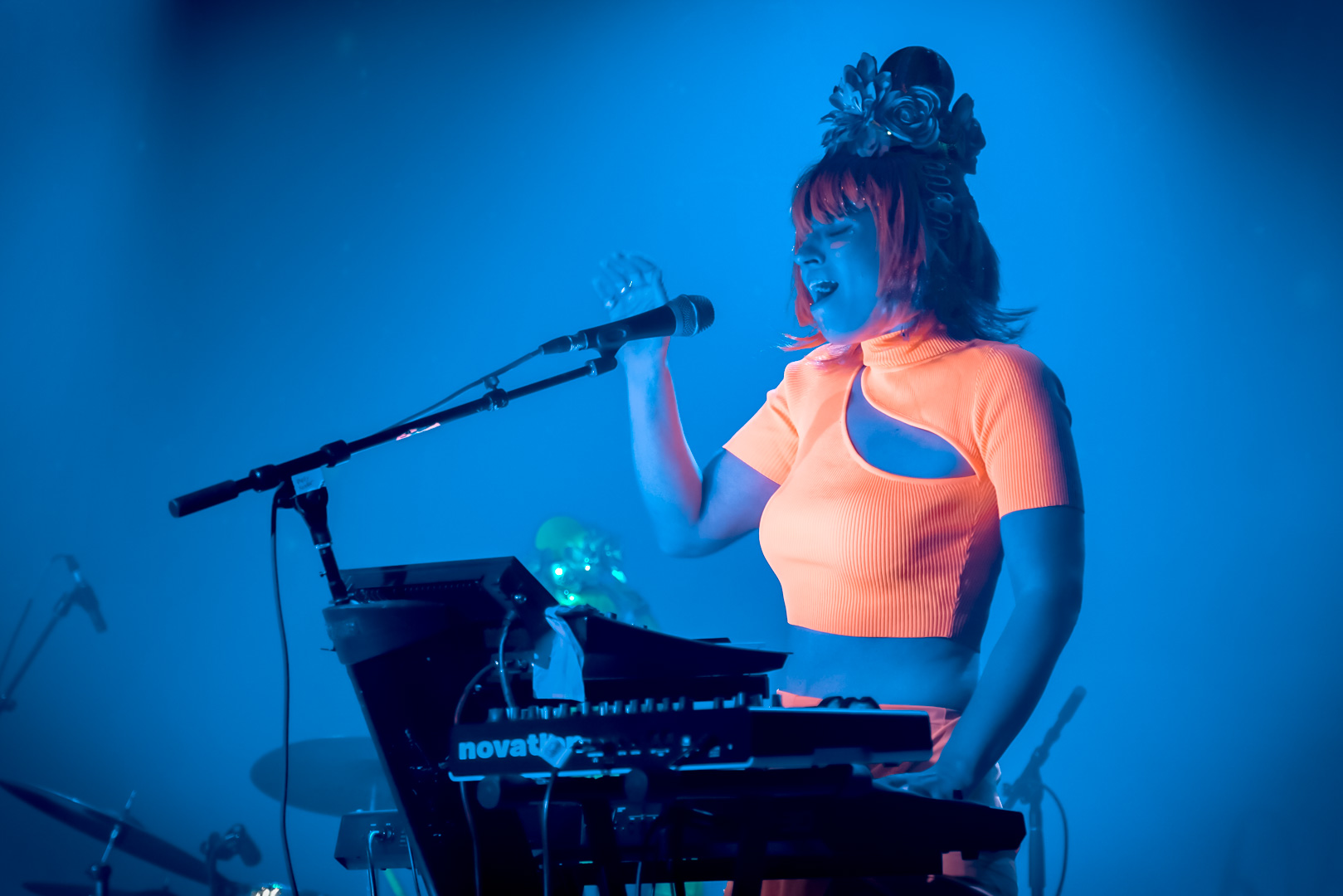 A woman in orange neon outfit playing keyboard and singing