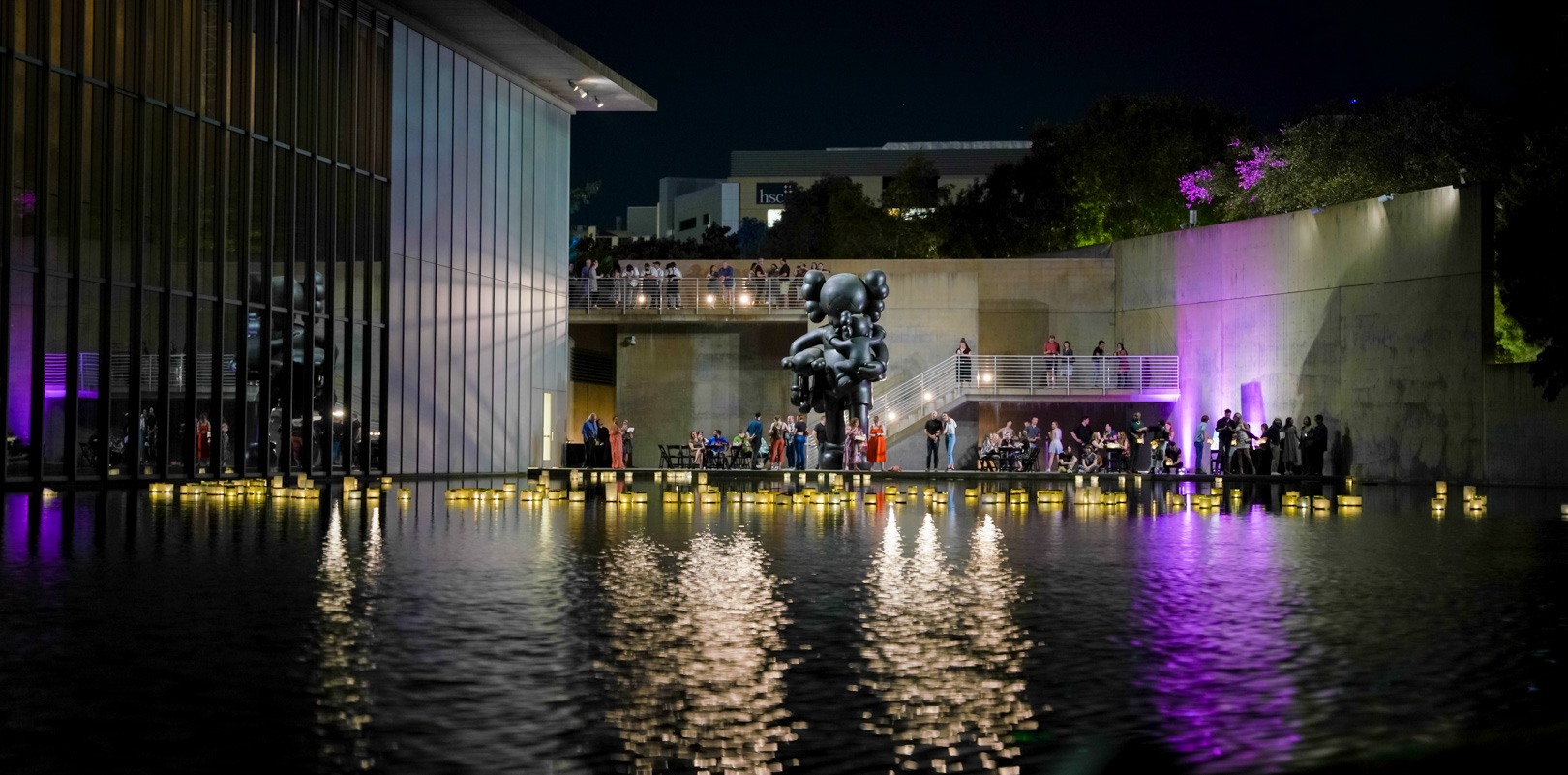 A reflecting pond with lanterns lit in front of a large sculpture