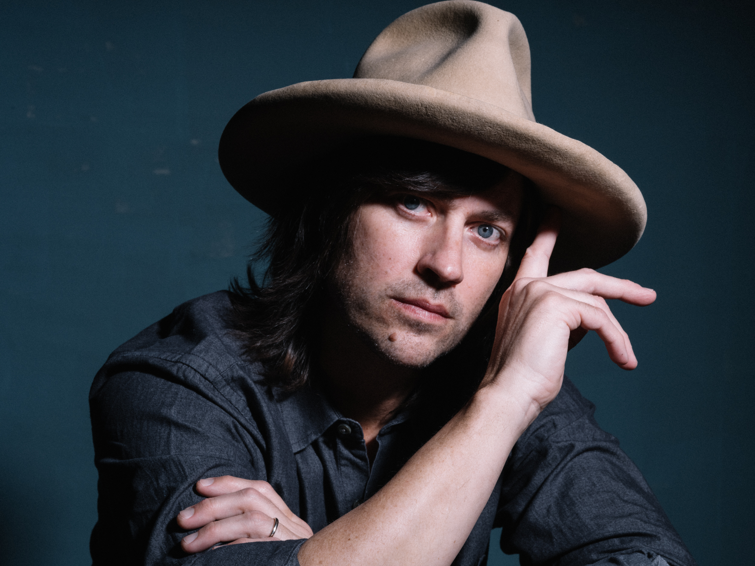 With a fedora on his head, Rhett Miller, in a dark shirt, looks at the camera