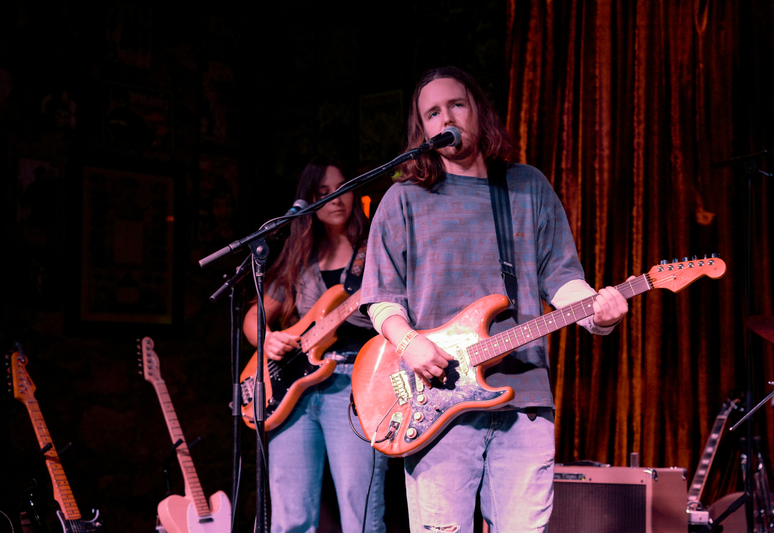 A man playing guitar and singing, a woman behind him playing bass