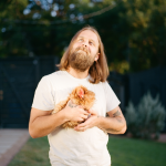 Brody Price, wearing a white T-shirt and holding a chicken, looks off to the left