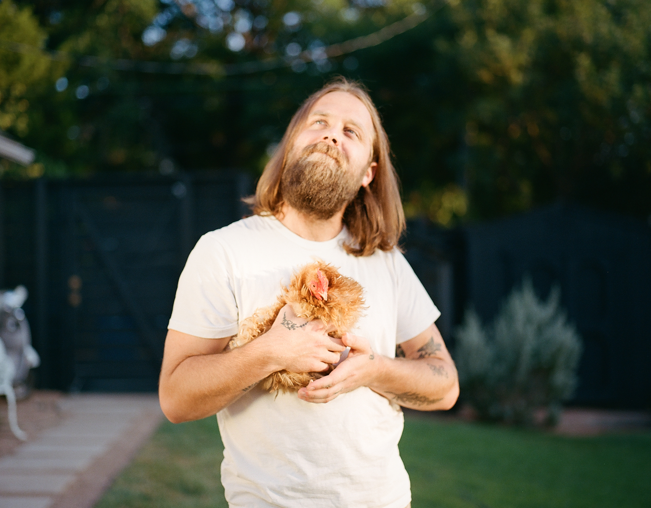 Brody Price, wearing a white T-shirt and holding a chicken, looks off to the left