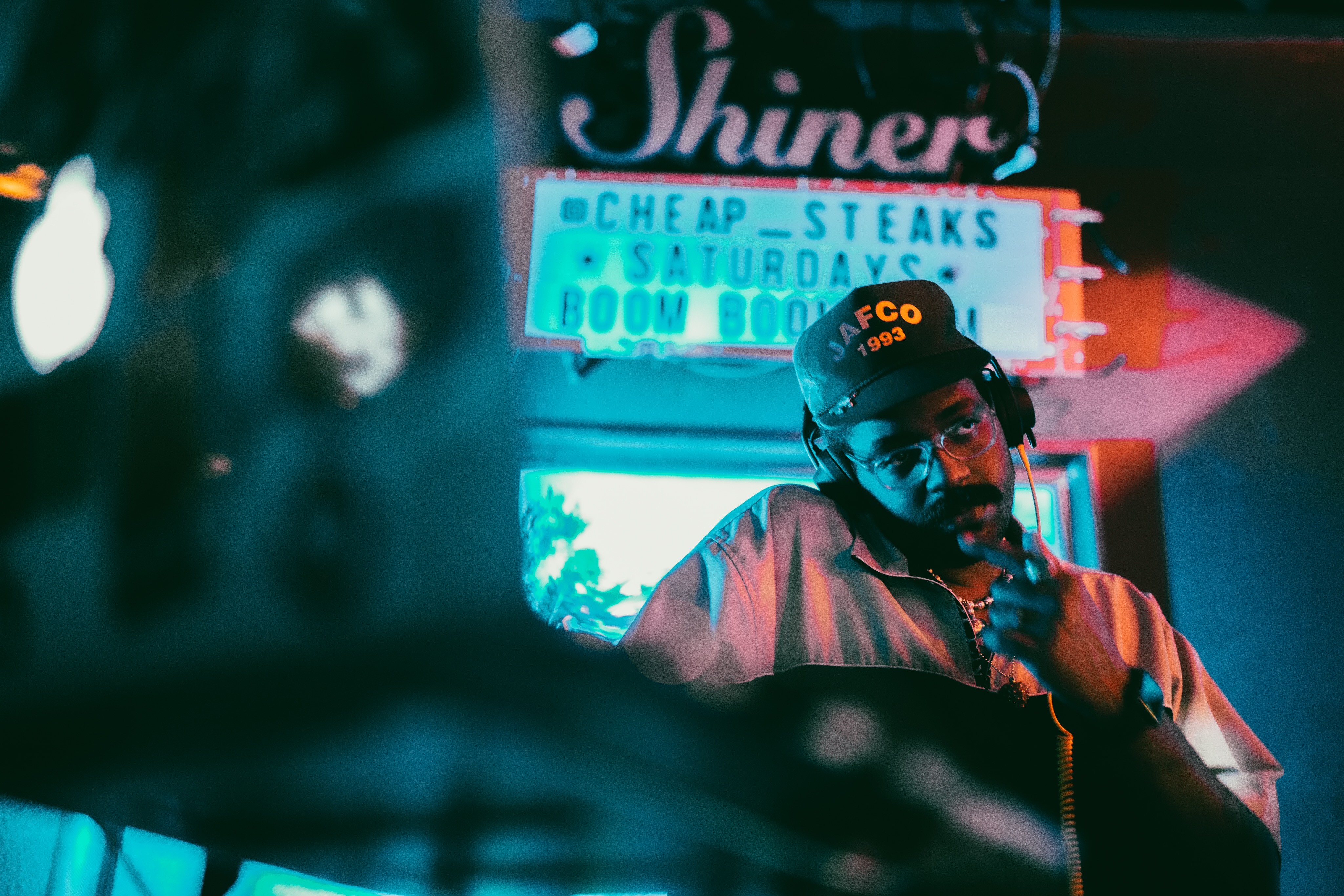 DJ Boyblk, wearing a baseball cap, mans a turntable inside a club