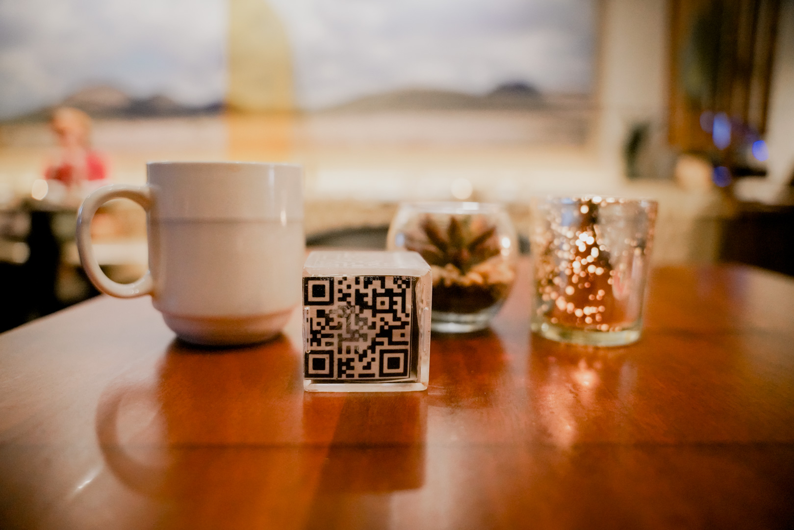 A coffee cup, succulent, candle and cube with a QR code on a table