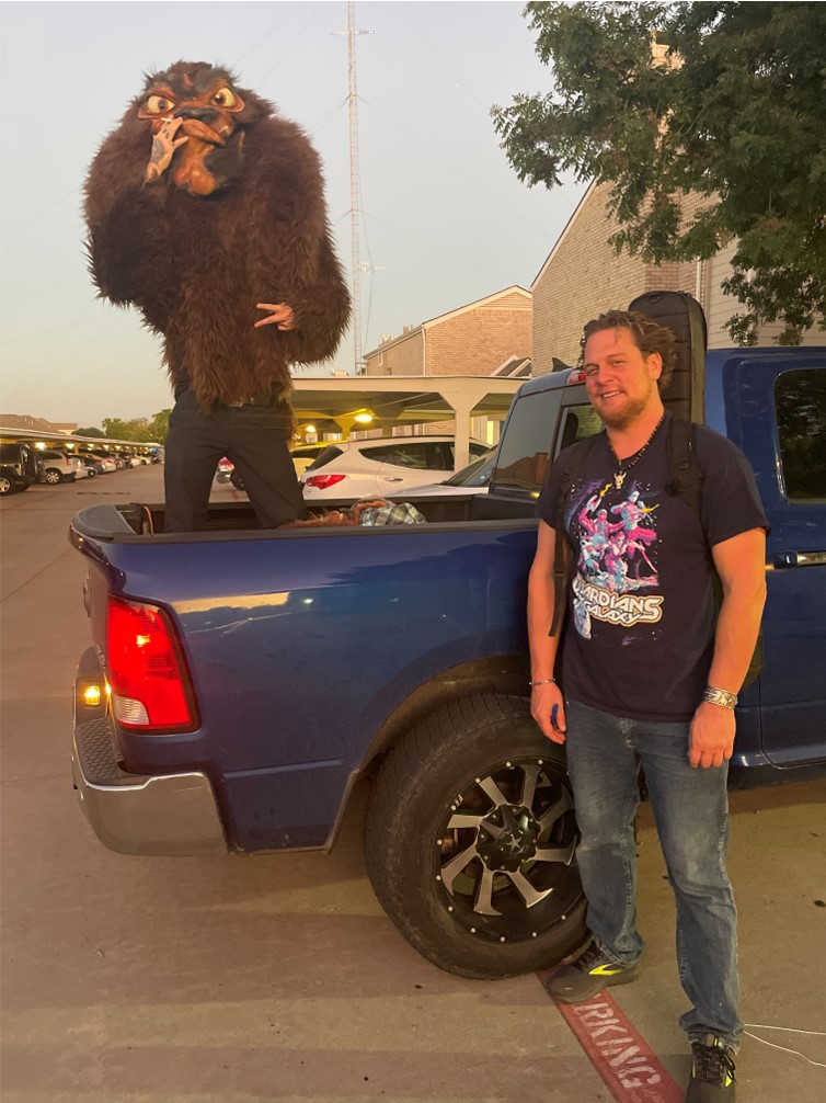 A man standing bext to a pickup truck and another man in a monster costume
