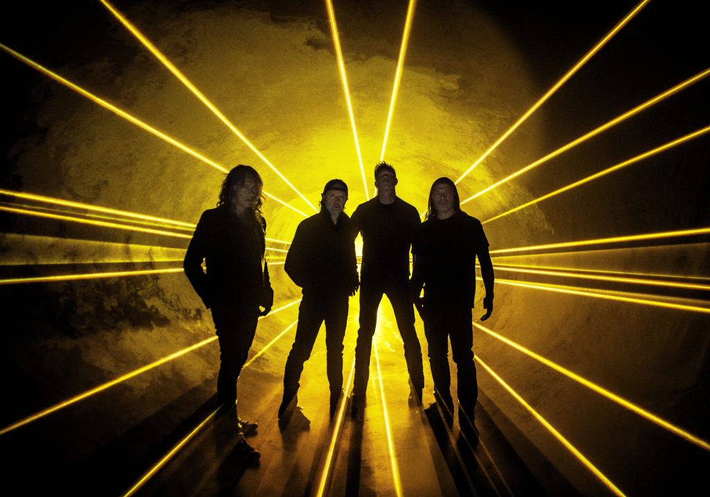 Backed by yellow lights, the four members of Metallica stand, shrouded in darkness