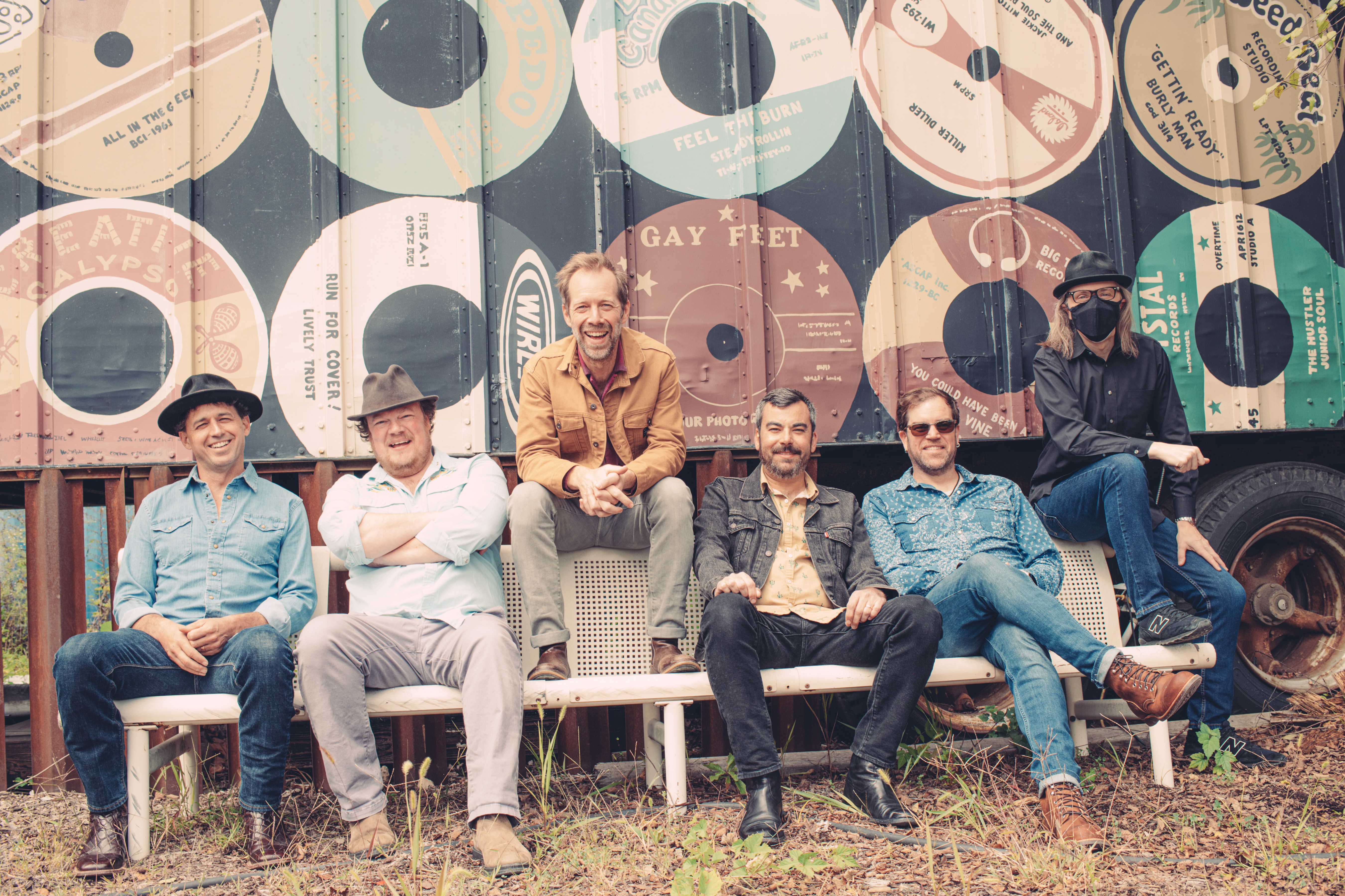 The six members of Steep Canyon Rangers sit in front of a barn wall, painted with images of 78s