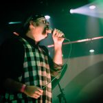 A man on stage singing into microphone, profile view