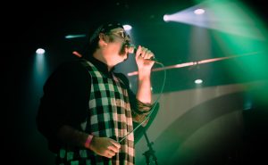 A man on stage singing into microphone, profile view