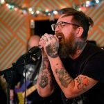 A man with tattoos sings passionately into a microphone
