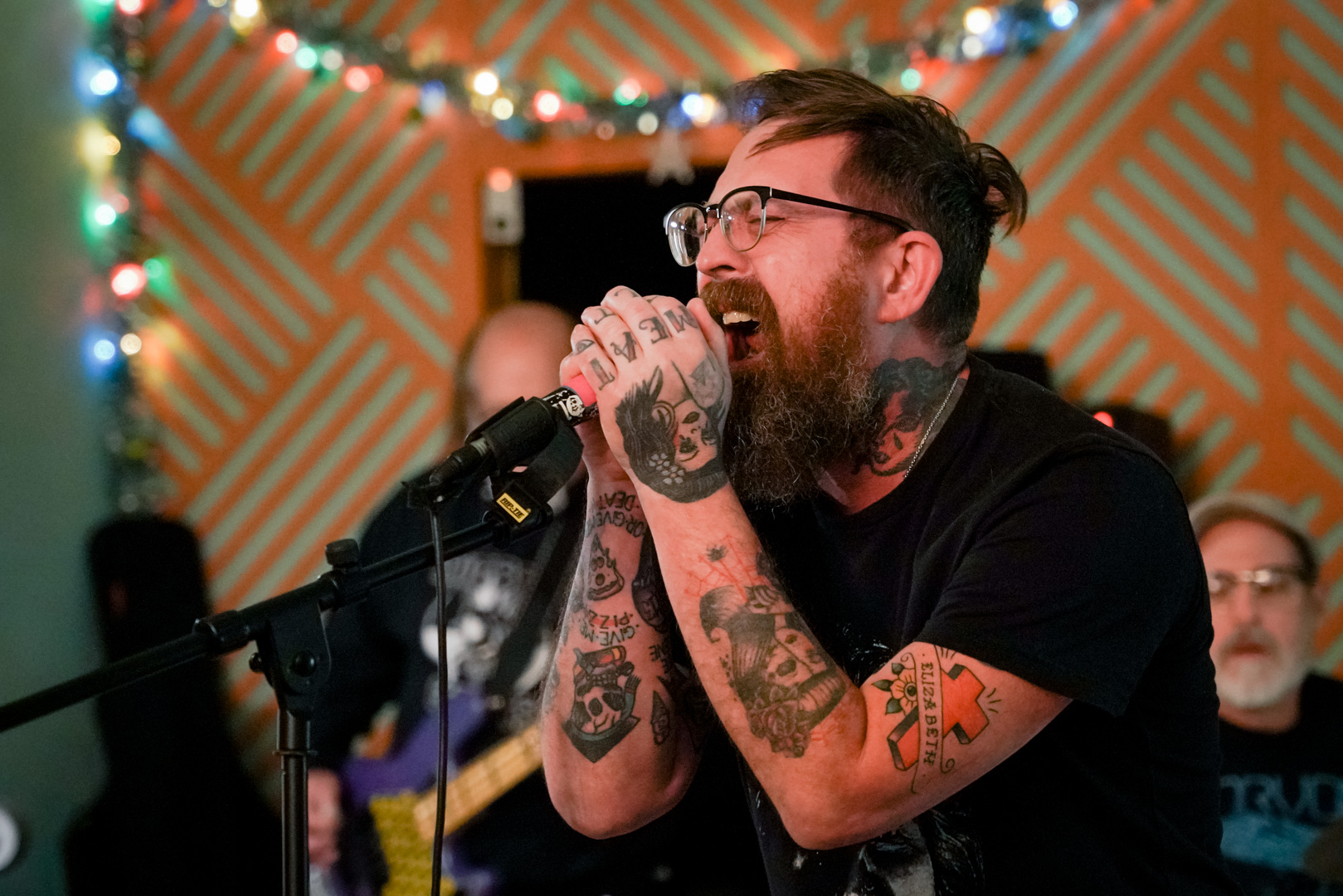 A man with tattoos sings passionately into a microphone 
