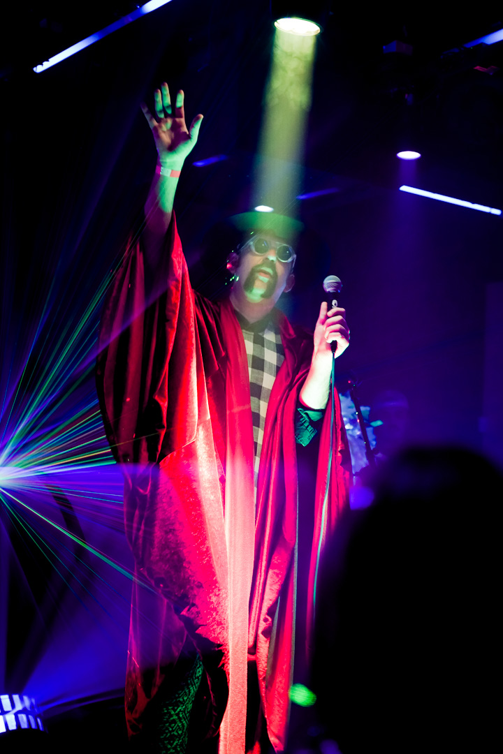 A man on stage in a robe with one hand up and the other holding a microphone