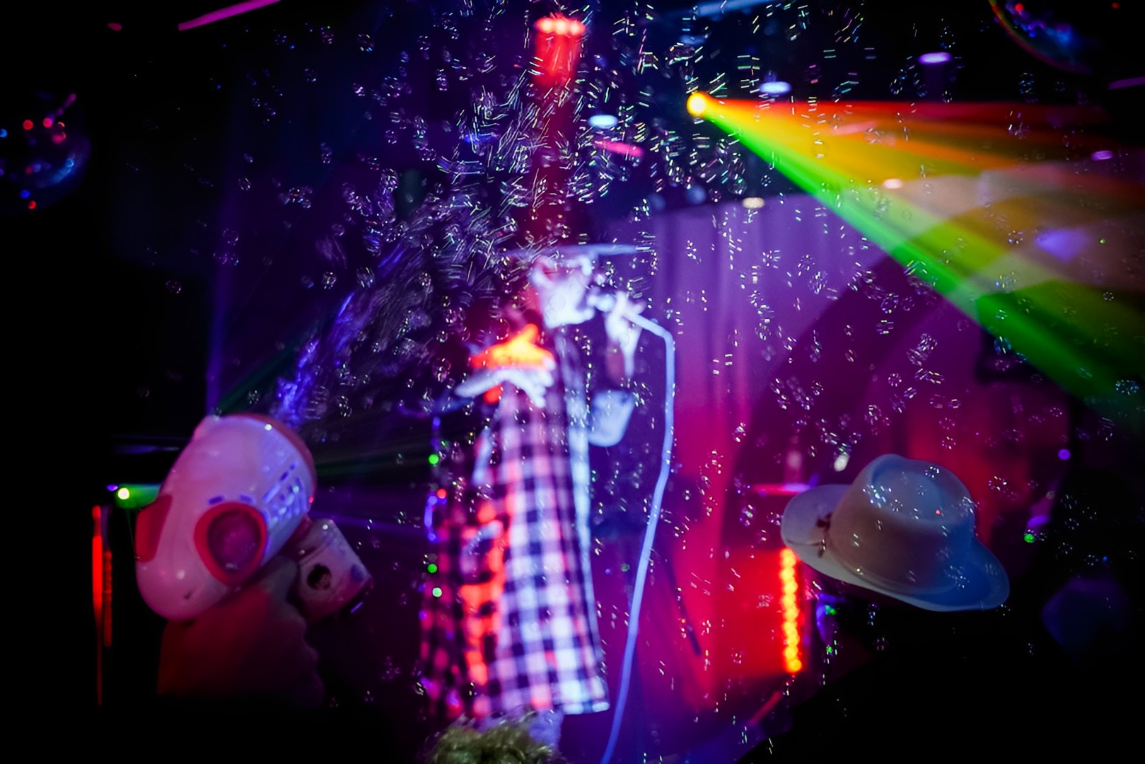 A hand holding a bubble gun, a single blurred in the background on stage