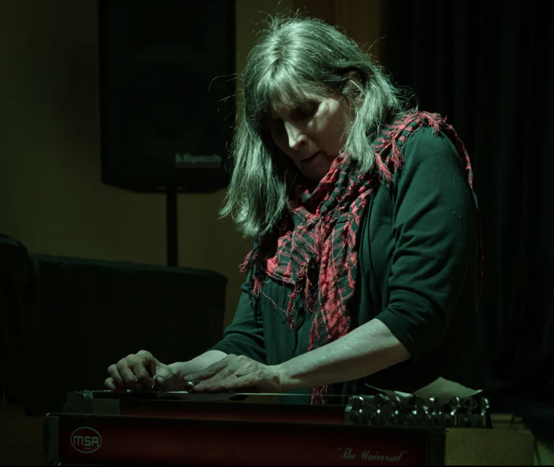 Susan Alcorn, wearing a dark shirt and a red scarf, plays the pedal steel