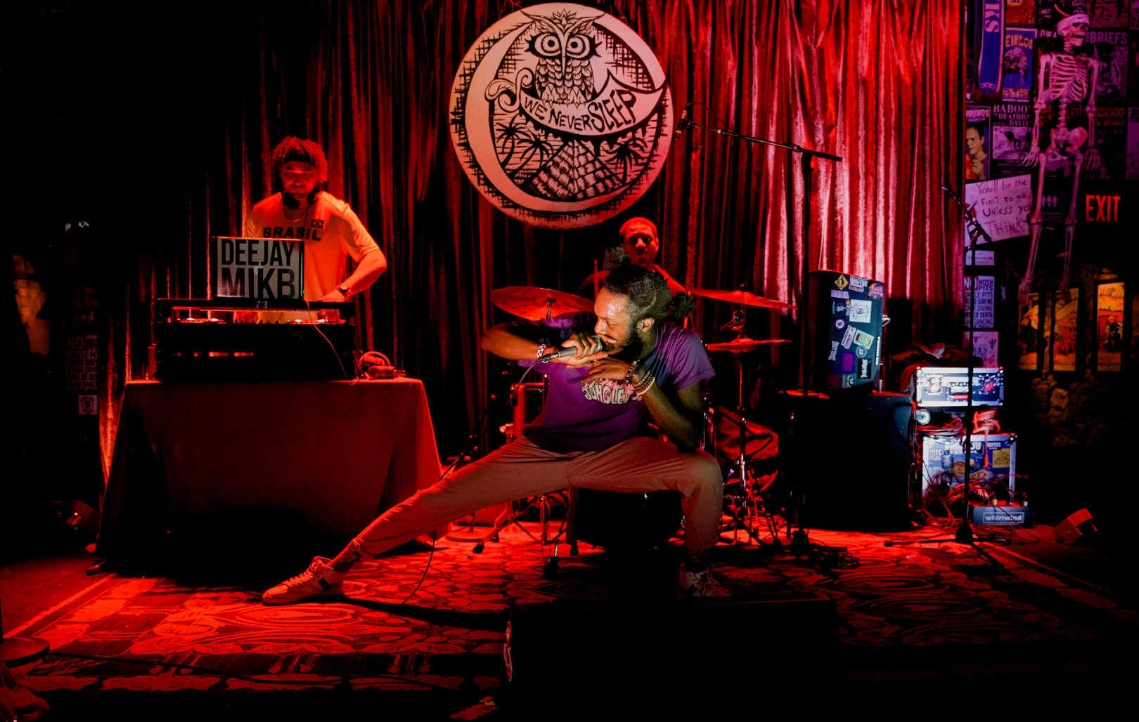 A full band on stage, singer low to ground in a wide-stanced crouch position